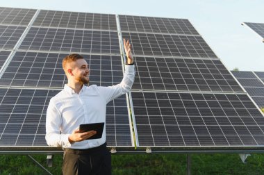 Yenilenebilir enerji projesi yönetimi için dijital tablet kullanan bir güneş çiftliğinde sürdürülebilir enerji üretimi planlayan mühendis