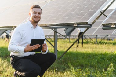 Bir güneş çiftliğindeki yenilenebilir enerji üretimini izlerken gülümseyen genç bir adam. Sürdürülebilirlik ve yeşil enerji kavramı