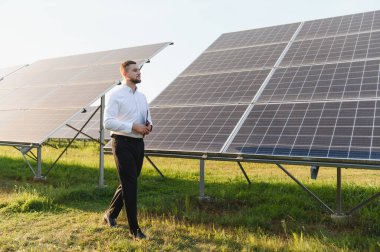 Bir güneş çiftliğinde elinde tablet olan ve fotovoltaik panelleri inceleyen erkek mühendis. Yeşil enerji ve sürdürülebilirlik kavramı