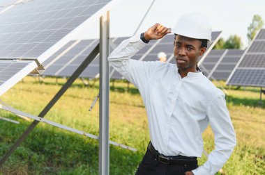 Şapkalı genç bir adam güneş paneli sahasında duruyor. Yenilenebilir enerji ve sürdürülebilirlik kavramı