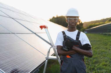 Güneş çiftliğinde elinde matkap tutan erkek teknisyen sürdürülebilir yenilenebilir enerji üretimine katkıda bulunuyor.