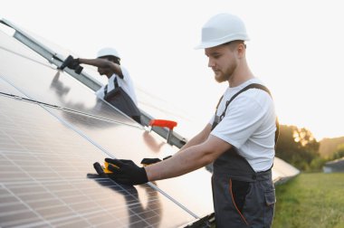 Mühendisler sürdürülebilir elektrik için güneş panelleri kuruyor. Güneşli bir günde yenilenebilir enerji çözümlerine katkıda bulunuyorlar.