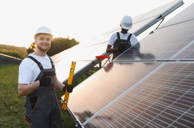 Güvenlik kaskı ve tulum takan mühendisler güneş panelleri kurarak verimli yeşil enerji üretimini sağlıyorlar.