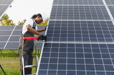 Afrika kökenli Amerikalı erkek teknisyen güneş panelleri kuruyor, yeşil enerji üretimine ve sürdürülebilir enerji çözümlerine katkıda bulunuyor