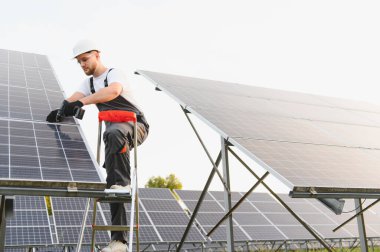 Bir güneş paneli dizisi üzerinde çalışan mühendis, ticari bir güneş çiftliğinde yenilenebilir enerji sistemi için elementler kuruyor.