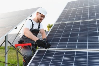 Sert şapka ve güvenlik gözlüklü teknisyen güneş alanına fotovoltaik modüller yerleştiriyor ve temiz enerji üretiyor.