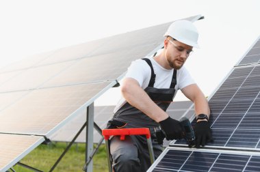 Erkek mühendis güneş panelleri kuruyor açık havada bir elektrikli matkap kullanarak, sürdürülebilir yenilenebilir enerjiye katkı sağlıyor