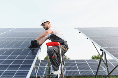 Koruyucu üniforma ve kask giyen işçiler güneş panelleri kuruyor, yeşil güç üretimine katkıda bulunuyor