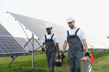 Çeşitli mühendisler araçlar ve merdiven taşıyarak yenilenebilir enerji çiftliğinde sıra sıra güneş panellerinden geçerek yeşil enerji üzerinde çalışıyorlar.
