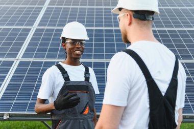 Güneş paneli alanında sabit şapka ve güvenlik gözlüğü takan çeşitli mühendisler yenilenebilir enerji çözümleri ve teknolojiyi tartışıyorlar.