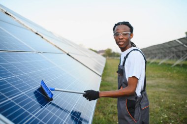 Genç adam güneş panellerini temizliyor, güneş enerjisi santralinde bakım yapıyor. Yenilenebilir enerji tanıtımı