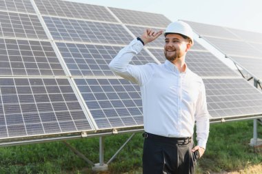 Güneş alanını denetleyen, yenilenebilir enerji ve sürdürülebilirliği destekleyen mühendis. Beyaz gömlekli ve kasklı profesyonel
