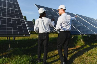 İki mühendis, yenilenebilir enerji çiftliğinde güneş panellerini inceliyor. Temiz enerji çözümleri geliştiriliyor
