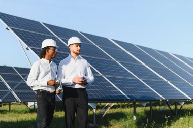 Güneş paneli alanında duran iki farklı mühendis yenilenebilir enerji ve sürdürülebilirlik çözümlerini tartışıyor.