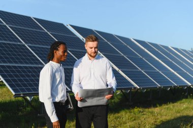 İki farklı mühendis yenilenebilir enerji geliştirme üzerinde çalışan sürdürülebilir bir güneş çiftliği planlarını tartışıyor.