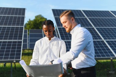 Çeşitli mühendisler, yenilenebilir enerji ve sürdürülebilirlik hedeflerini tartışarak, bir güneş enerjisi santralinin planlarını gözden geçiriyorlar.