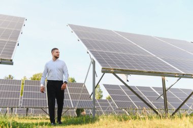 Güneş paneli çiftliğinde yürüyen erkek mühendis, sürdürülebilir enerji üretimi ve yeşil teknoloji çözümlerini kontrol ediyor