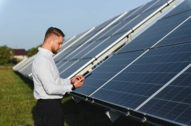 Yenilenebilir enerji yönetimi için dijital tablet kullanarak güneş paneli verimliliğini ve açık havada performansını izleyen genç mühendis