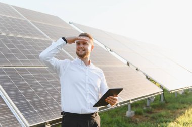 Güneş panellerini denetleyen tablet tutan erkek mühendis, gelecekteki sürdürülebilir enerji ve temiz teknolojiyi öngörüyor