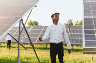 Afrika kökenli Amerikalı erkek mühendis güneş çiftliğinde dikilip fotovoltaik elektrik santralini denetliyor.