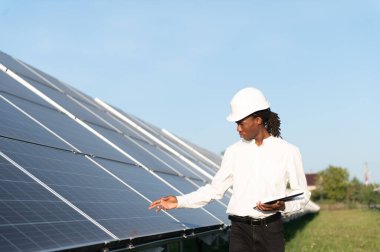 Sert şapkalı Afrikalı adam güneş panellerini denetliyor, verimli bir yeşil enerji üretimi sağlıyor. Temiz güç ve sürdürülebilirlik kavramı