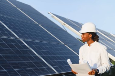 Katı şapka takan Afrikalı Amerikalı mühendis temiz enerji için güneş paneli kurulumunu denetliyor.