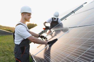 Bir güneş çiftliğine güneş panelleri kuran teknisyenler, temiz yenilenebilir enerji üretiyor ve sürdürülebilir kalkınmaya katkıda bulunuyor
