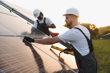 Sert şapka takan işçiler, güneş paneli sistemi kuruyorlar. Sürdürülebilirlik için güneş enerjisini yeşil elektrik enerjisine çevirmek