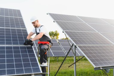 Bir güneş enerjisi santraline fotovoltaik paneller kurarak sürdürülebilir yeşil elektrik üreten güvenlik donanımı işçisi