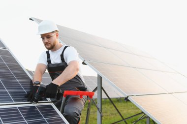 Fotovoltaik paneller kuran, yeşil enerjiye ve sürdürülebilir elektrik üretimine katkı sağlayan, sıkı şapkalı ve iş kıyafetli adam