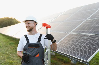 Güvenlik donanımlı mutlu işçiler yenilenebilir enerji için güneş panelleri kurarak sürdürülebilir enerjiye katkıda bulunuyorlar.