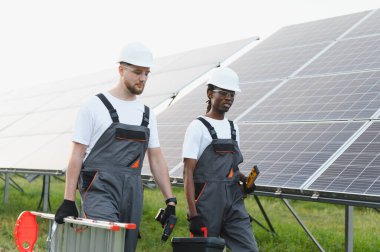 İki farklı mühendis, temiz yenilenebilir enerji yüklemek için güneş panelinde yürüyen araçlar ve bir merdiven taşıyorlar.
