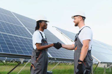 Çeşitli güneş enerjisi mühendisleri bir güneş enerjisi santralinde el sıkışıyor ortaklığı ve yenilenebilir proje başarısını simgeliyor.