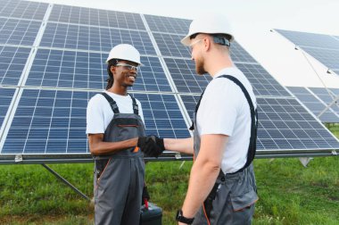 Çeşitli mühendislik ekipleri güneş enerjisi santralinde yeni yenilenebilir enerji ortaklığını kutluyor, el sıkışıyorlar ve gülümsüyorlar.