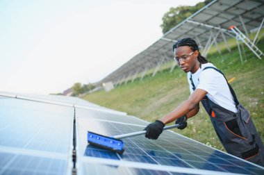 Büyük bir güneş çiftliğinde güneş paneli yüzeyini temizleyen Afrikalı Amerikalı teknisyen optimum yenilenebilir enerji üretimini sağlıyordu.