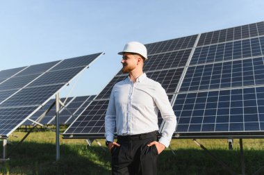 Genç erkek mühendis güneş paneli alanında dikilip temiz yenilenebilir enerji üretimi sağlıyor.