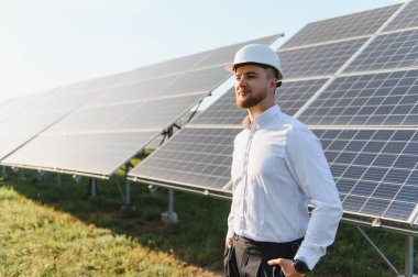 Fotovoltaik enerji istasyonundaki güneş panellerini inceleyen genç adam, sürdürülebilir enerji üretimine odaklanıyor