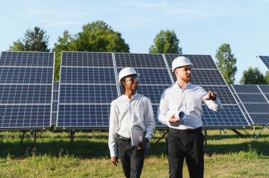 Güneş paneli alanında yürüyen iki farklı mühendis yenilenebilir enerjiyi tartışıyor ve alanı inceliyor.
