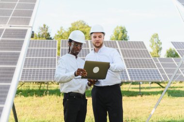 Sert şapkalar takan iki mühendis güneş çiftliğindeki bir laptoptan verileri kontrol ediyor ve sürdürülebilir enerjiye odaklanıyor.