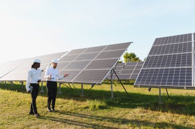 Sert şapkalı mühendisler güneş paneli alanındaki çalışmaları inceleyip tartışıyorlar, yenilenebilir enerji ve yeşil teknolojiye odaklanıyorlar.