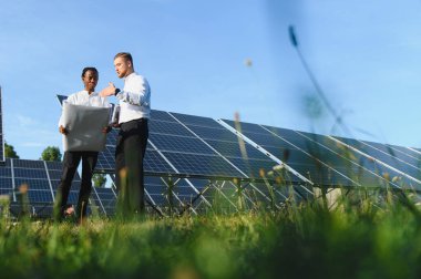 Çeşitli mühendisler güneş paneli alanındaki planı gözden geçirip yenilenebilir enerji ve sürdürülebilir teknolojiyi tartışıyorlar.