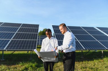 İki farklı mühendis planlarını tartışıyor ve güneş panelleriyle çalışıyor, yenilenebilir enerji ve sürdürülebilir kalkınma üzerine odaklanıyorlar