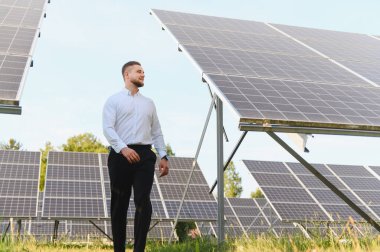 Güneş panelleri arasında yürüyen genç işadamı, sürdürülebilir enerji çözümleri ve yenilenebilir enerjiyi simgeliyor