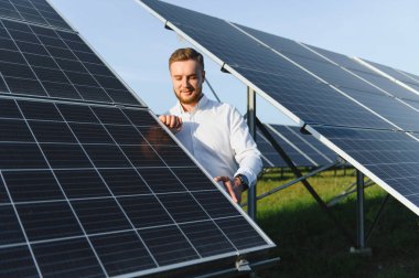 Bir güneş çiftliğinde duran genç mühendis, güneş panellerini denetliyor ve yeşil enerji sisteminin optimal işleyişini sağlıyor.