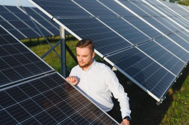 Ticari bir güneş enerjisi çiftliğinde çalışan erkek mühendis, temiz enerji üretimini ve sürdürülebilir teknolojiyi kontrol ediyor