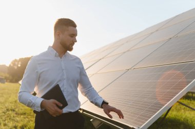 Genç adam tablet kullanıyor, fotovoltaik panelleri kontrol ediyor. Yenilenebilir enerji, sürdürülebilirlik ve yeşil teknolojinin vurgulanması