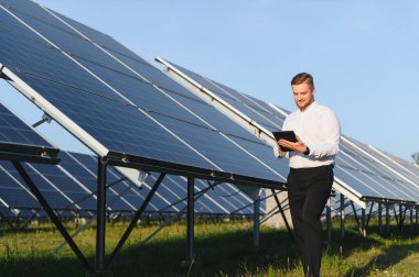 Veri izleme ve sürdürülebilir enerji yönetimi için dijital tablet kullanan adam güneş panelleri alanını denetliyor
