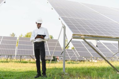 Yenilenebilir enerji çiftliğindeki güneş panellerini kontrol ederken dijital tablet kullanan Afrika kökenli Amerikalı mühendis.
