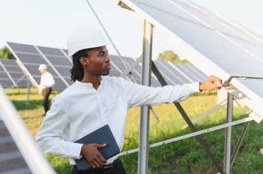 Büyük bir güneş enerjisi santralinde güneş modüllerini denetleyen sert şapka takan genç mühendis elinde bir tablet tutuyordu.