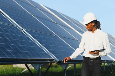Güneş panellerini teftiş eden, elinde bir tablet tutan, sürdürülebilir enerji üretimine odaklanan Afrika kökenli Amerikalı mühendis.